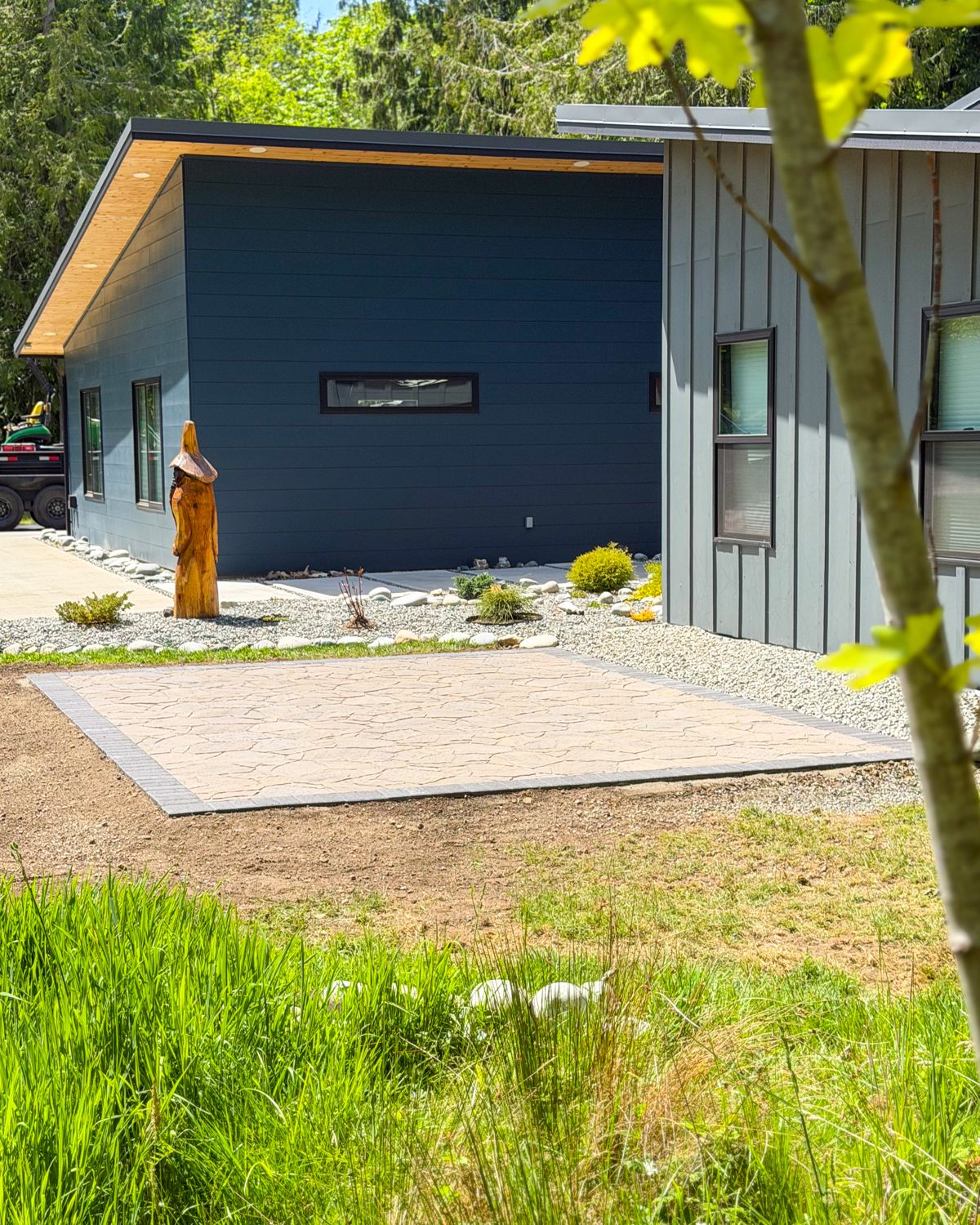 Square paver patio with a charcoal border beside a modern dark-blue home